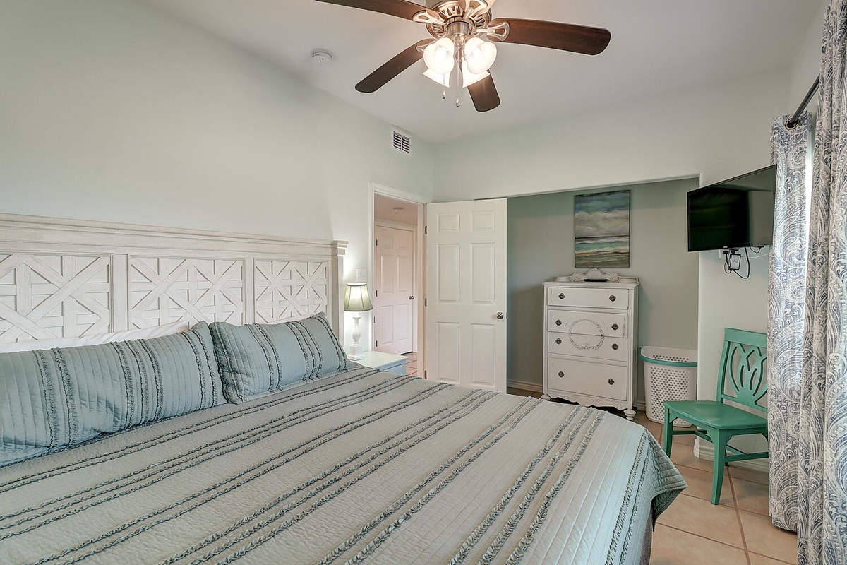 Relax in your coastal-themed bedroom with soothing teal bedding, rustic white headboard, and ceiling fan for your comfort.