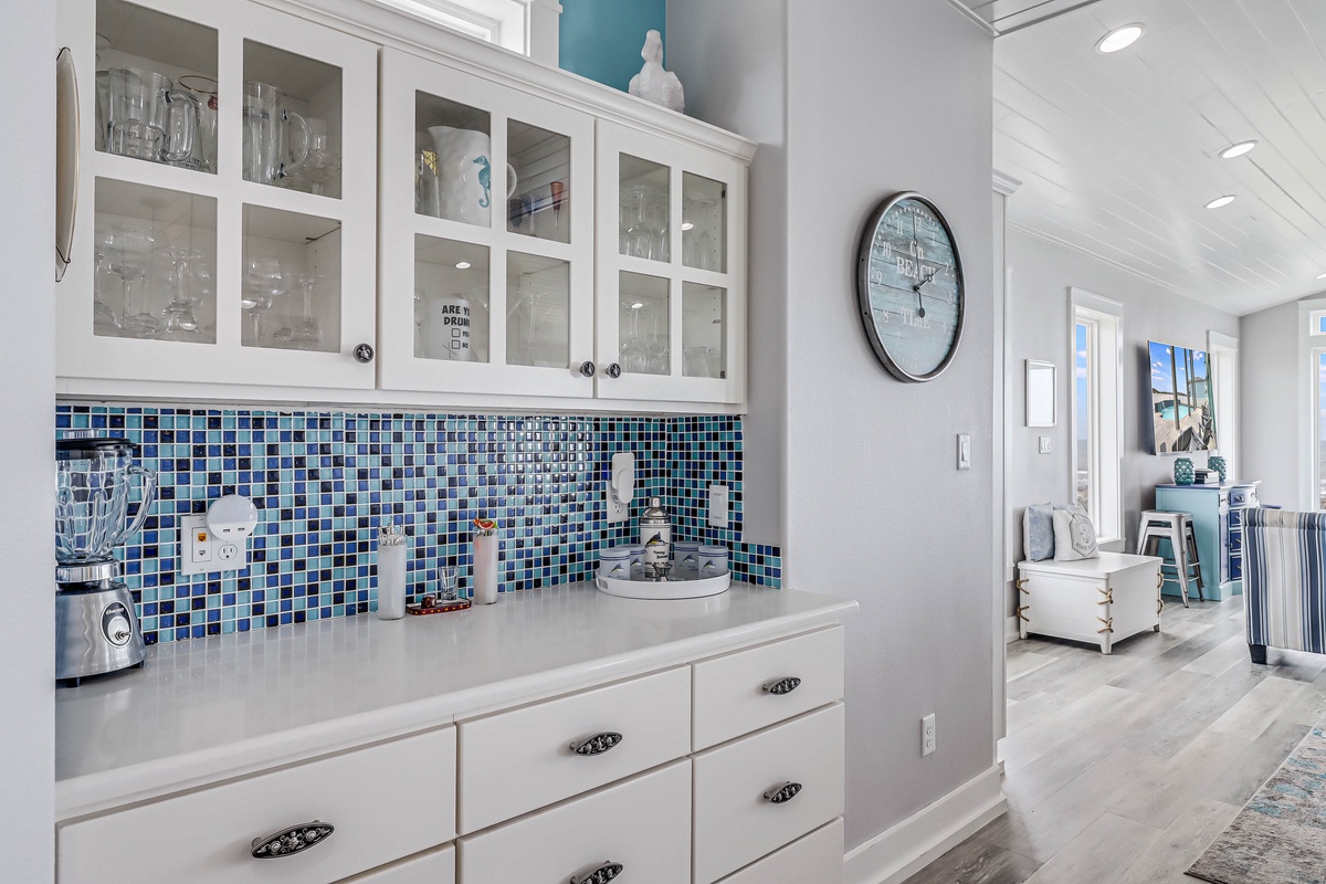 Your stylish kitchenette features stunning blue mosaic tile backsplash, glass-front cabinets displaying dishes, and modern appliances for convenient meal prep.