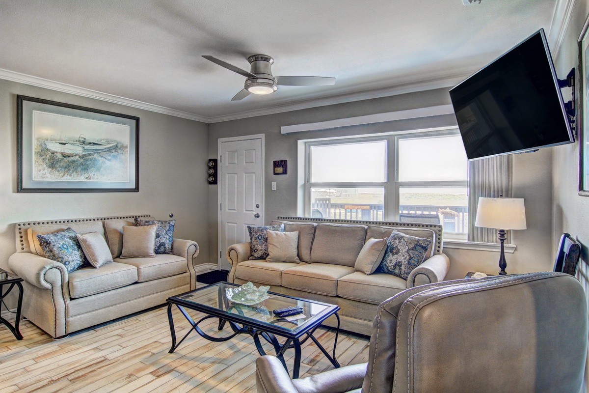 Settle into your comfortable living room with plush seating, coastal artwork, and natural light streaming through large windows.