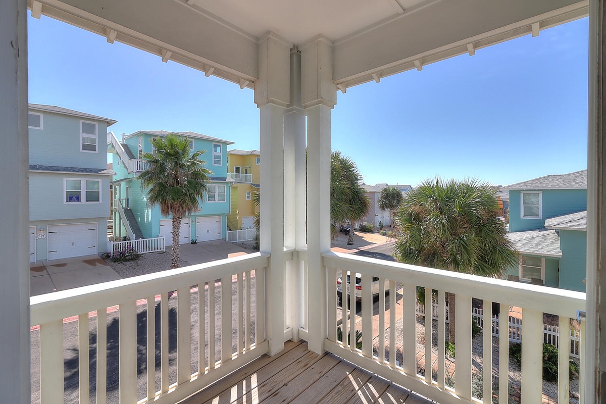 Colorful beachside neighborhood view from covered porch with tropical palms and coastal architecture.