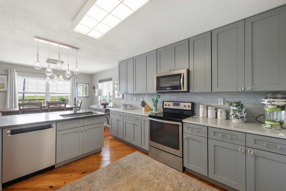 Step into your bright, airy kitchen with soft gray cabinetry, gleaming countertops, and natural light pouring through the skylight—perfect for preparing meals while enjoying the open, inviting atmosphere.