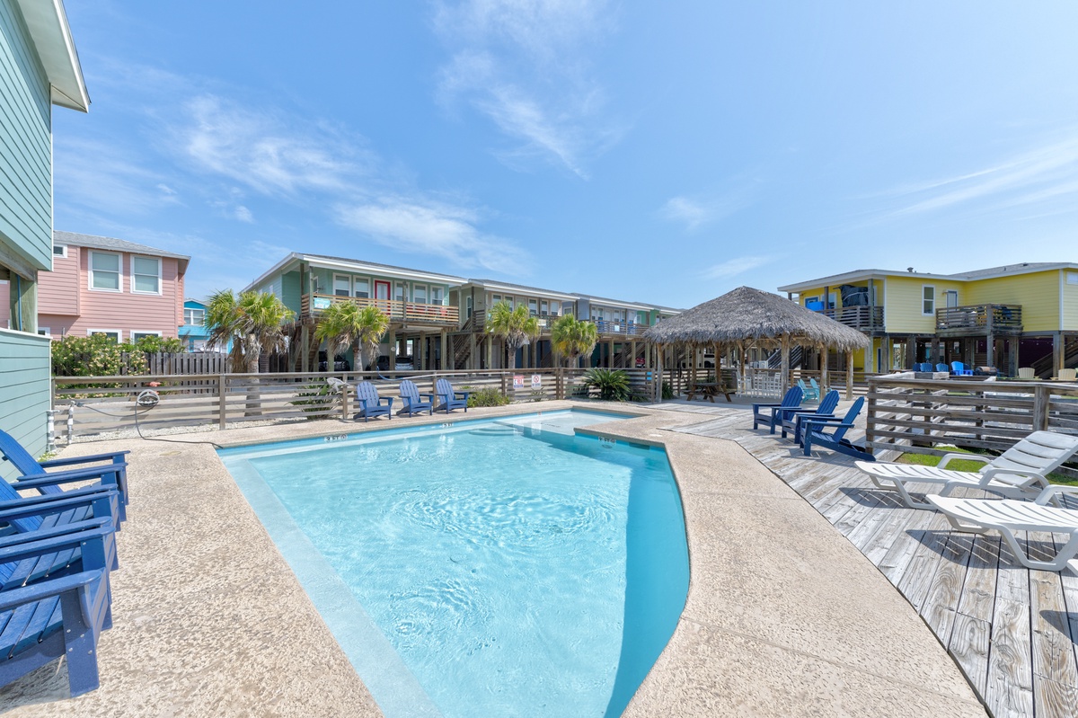 A vibrant coastal resort community surrounds the pool area, with colorful beach houses and a thatched palapa defining the property's relaxed island atmosphere.