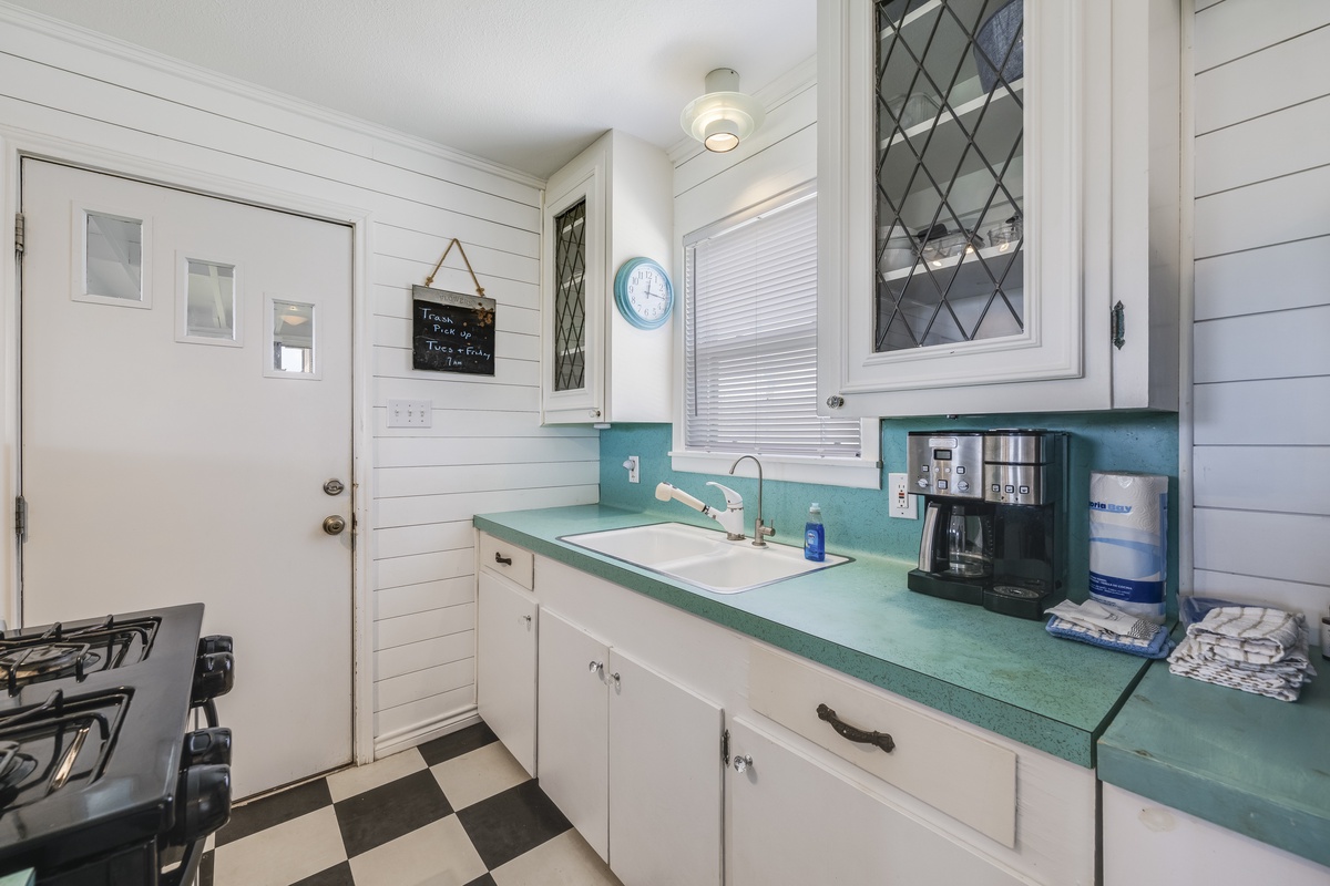 Your bright, retro-style kitchen features turquoise countertops, white shiplap walls, and checkered floors. Everything you need—coffee maker, full-sized stove, and cozy charm—awaits your morning routine.