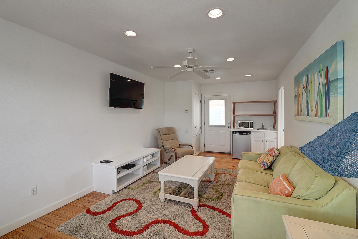 Relax in your bright, open living space with comfortable seating, modern kitchen, and charming coastal artwork creating the perfect beach getaway atmosphere.