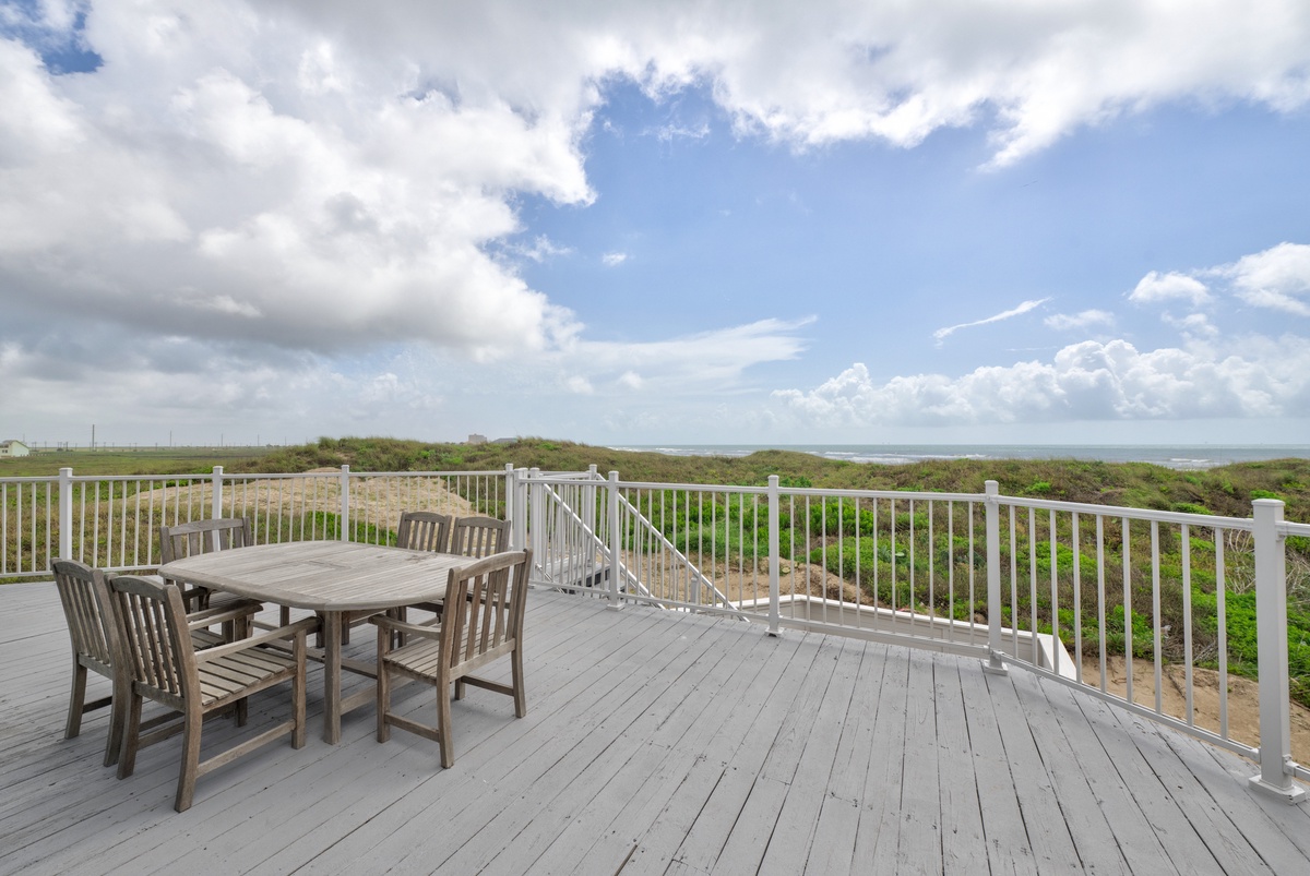 Expansive deck overlooking natural coastal landscape with comfortable dining area for memorable seaside meals.