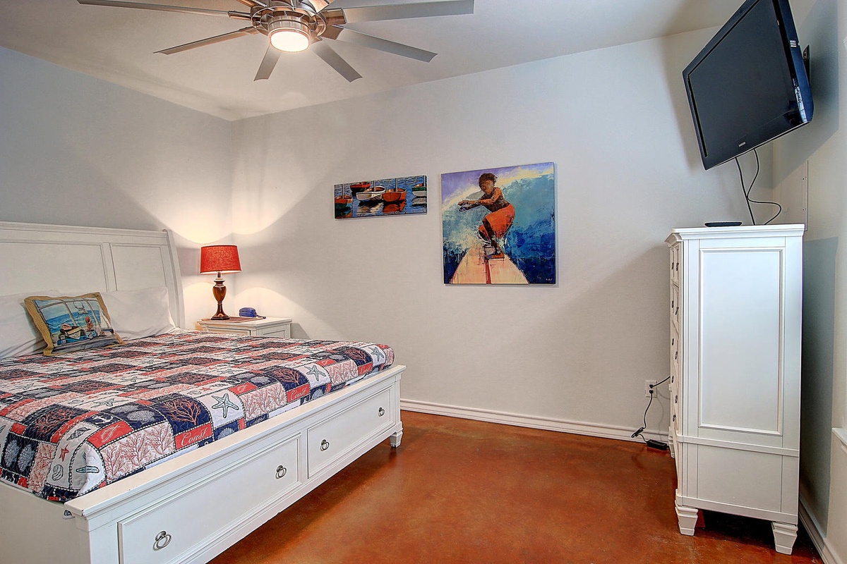 Your comfortable bedroom features a cozy bed, ceiling fan, and wall-mounted TV for relaxing evenings after beach adventures.