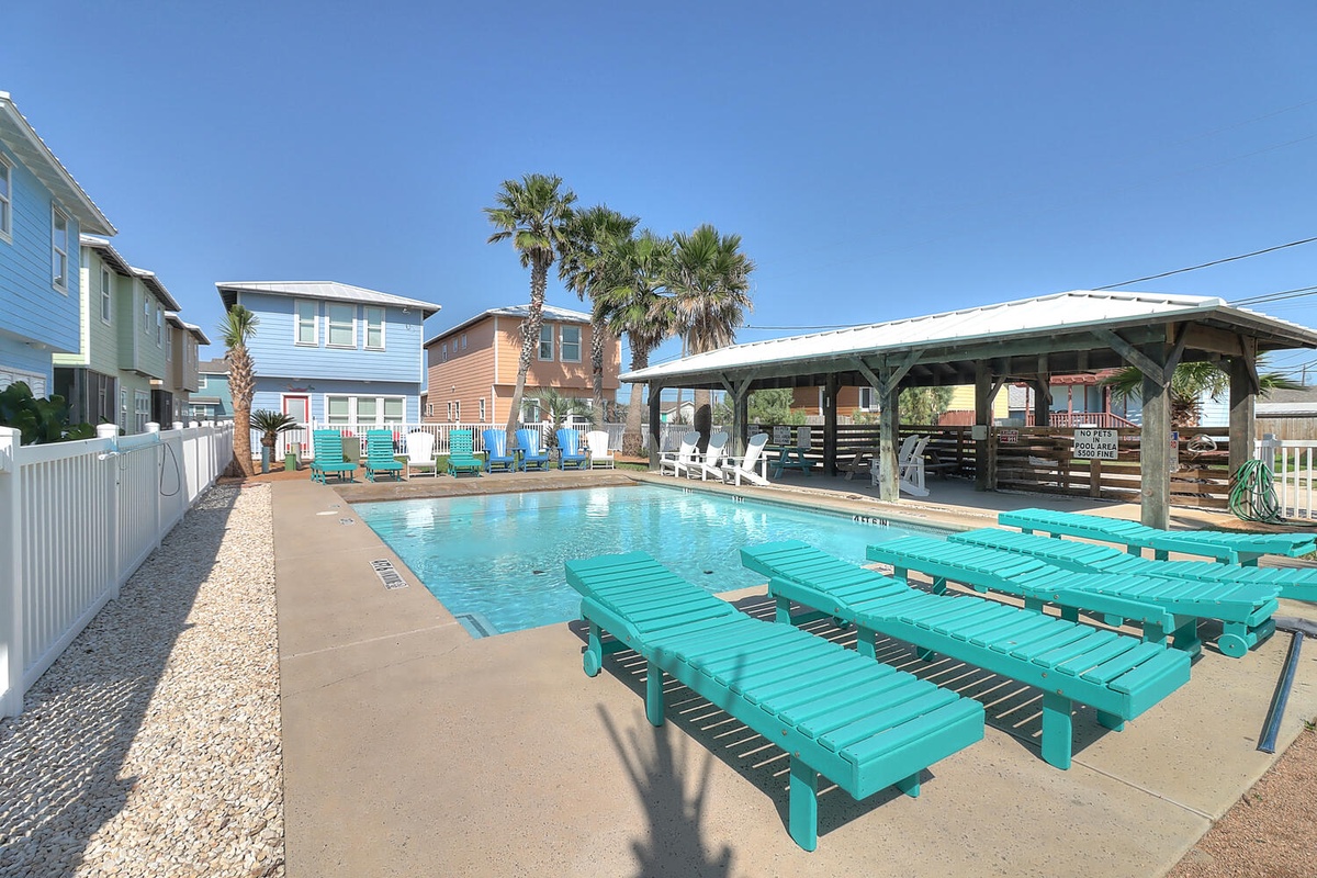Sparkling community pool surrounded by vibrant beach houses and swaying palm trees under endless blue skies.