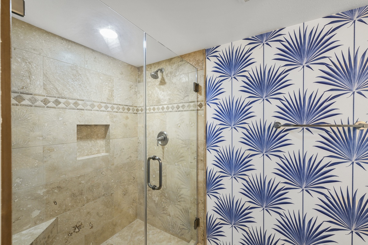 Step into your private sanctuary with a spacious walk-in shower featuring warm travertine tile and a striking tropical palm accent wall that brings coastal elegance to your daily routine.