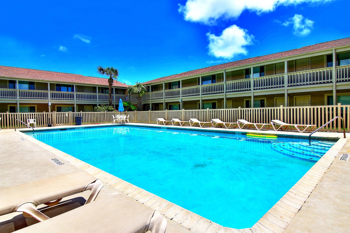 Crystal-clear pool surrounded by comfortable loungers creates your perfect sunny retreat under brilliant blue skies.