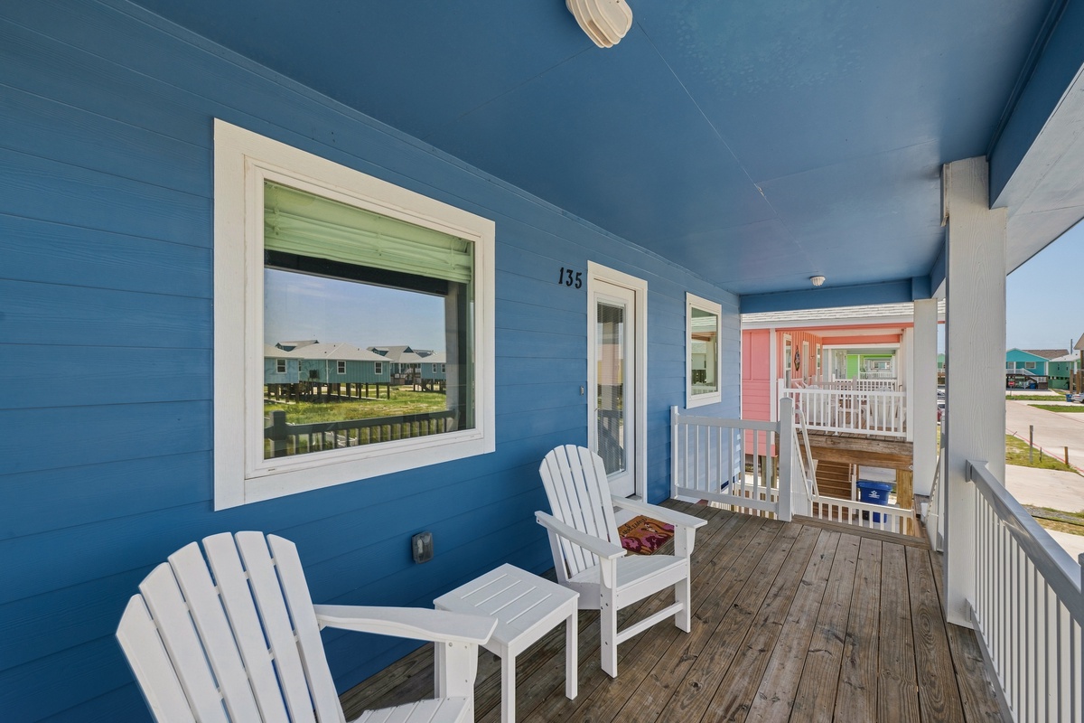 Your private porch invites you to settle into classic coastal comfort, where crisp blue walls and white Adirondack chairs frame peaceful neighborhood views.