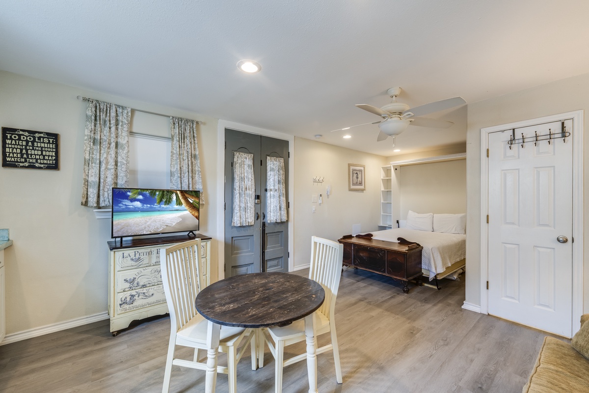 A bright, open studio welcomes you with coastal charm—ceiling fan, smart TV, cozy dining table, and plush bedding ready for your restful stay.