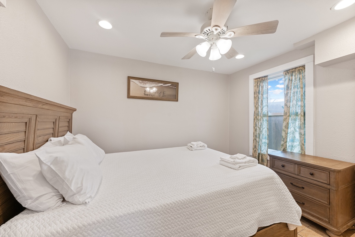 Sink into crisp white linens in your peaceful bedroom, where warm wood furnishings and gentle ceiling fan breezes create the perfect retreat.