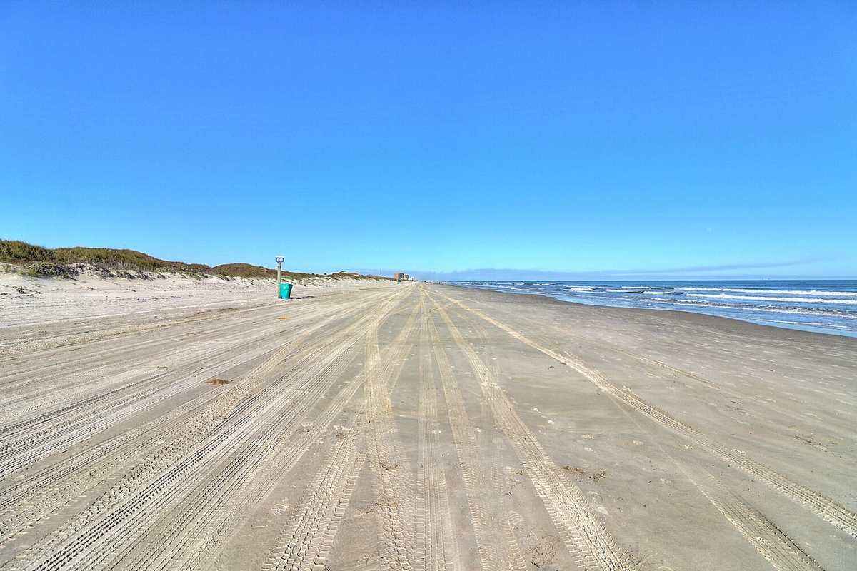 Expansive beach with pristine sand stretches along the coastline, featuring clear blue waters and natural dune vegetation.