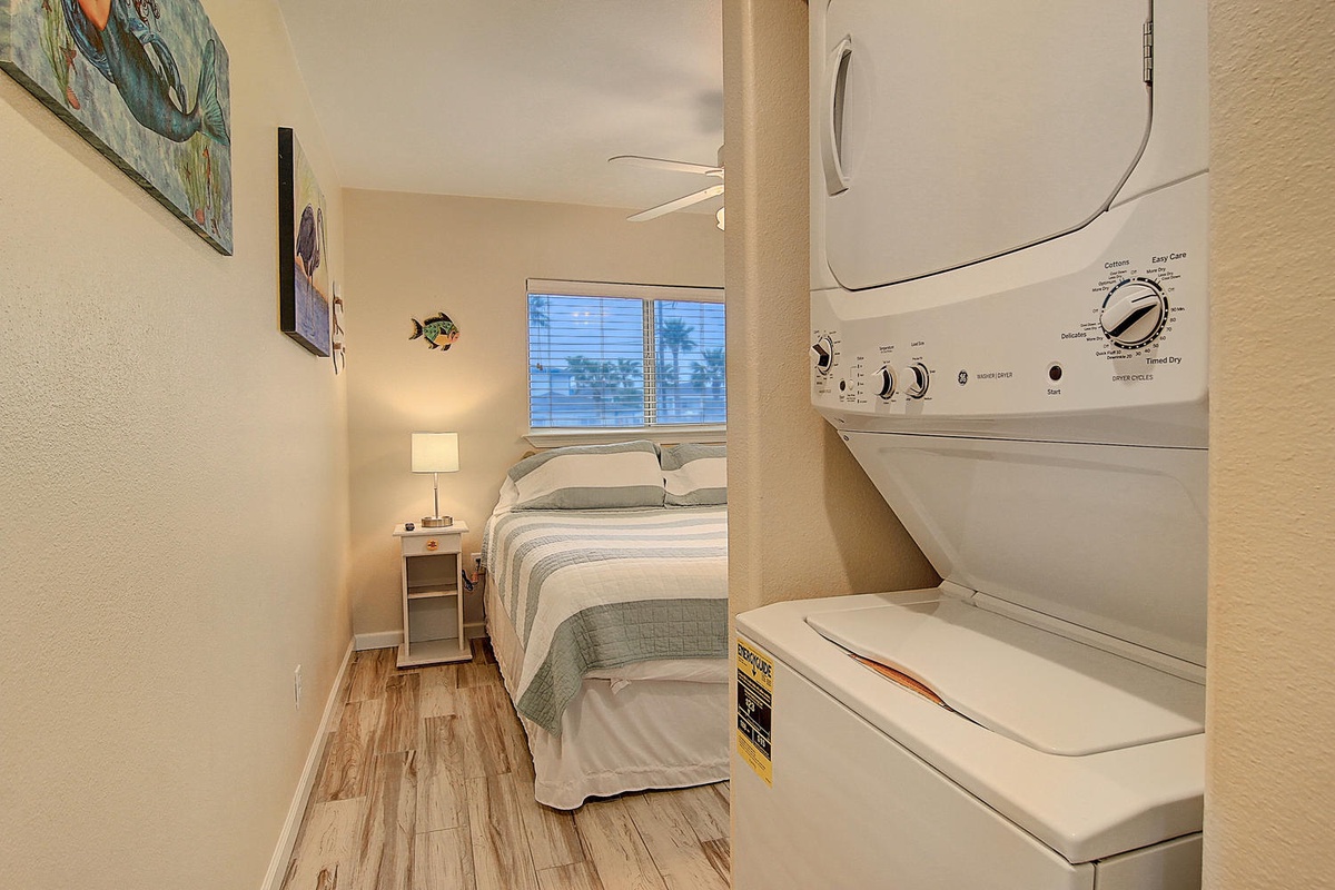 Your cozy bedroom features in-unit laundry convenience, with a comfortable bed and natural light streaming through the window.
