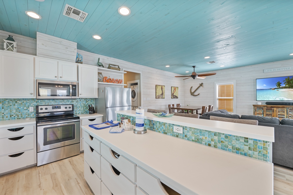 Step into your coastal retreat, where aqua-painted ceilings and turquoise tile backsplash capture the breezy charm of seaside living, blending a fully equipped kitchen and open living space for your comfort.