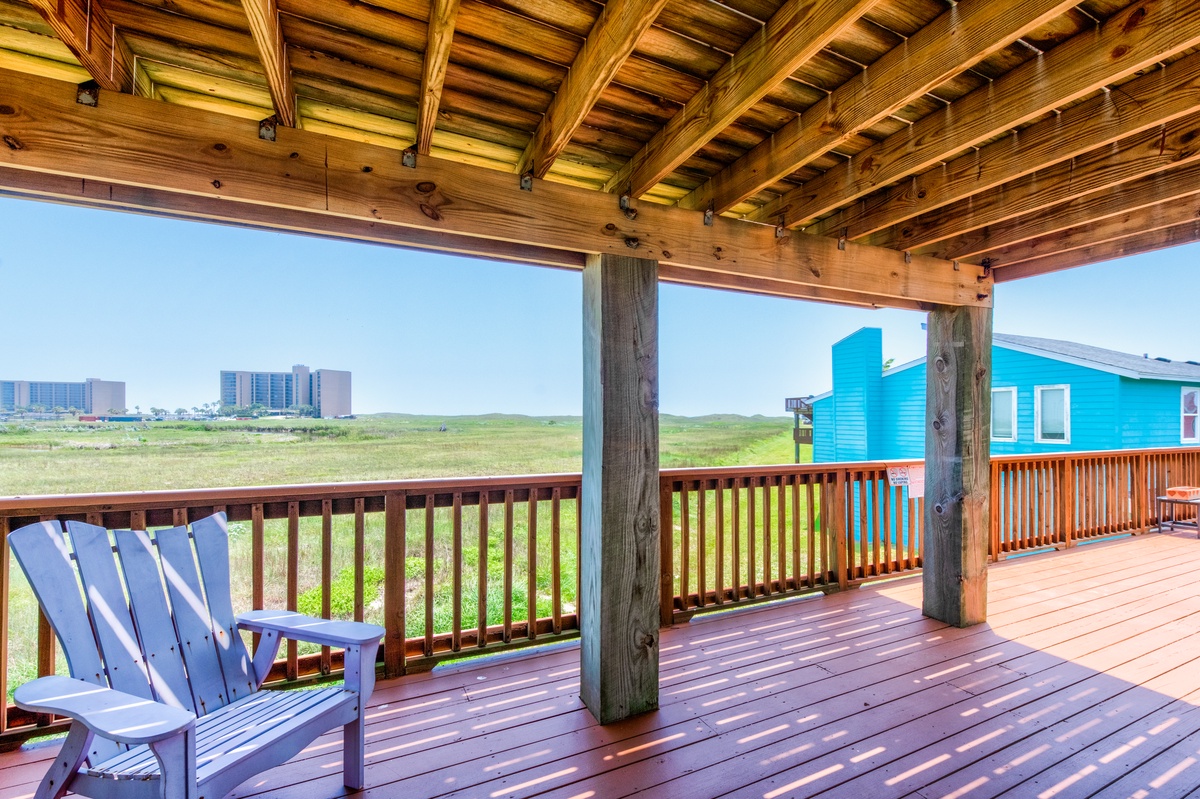 Relax on your private covered deck with sweeping views of the coastline, where Adirondack chairs invite peaceful moments under rustic beams.