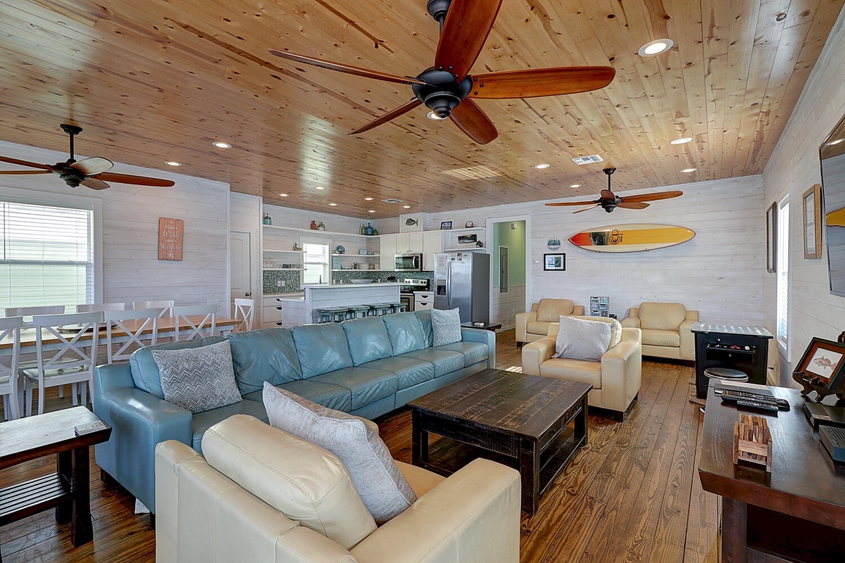 Relax in this stunning open-concept living space where coastal charm meets comfort beneath beautiful wood-planked ceilings and gentle ceiling fans.