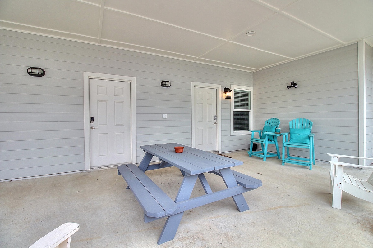 Your covered patio offers the perfect outdoor dining spot with a picnic table and colorful chairs for relaxing.