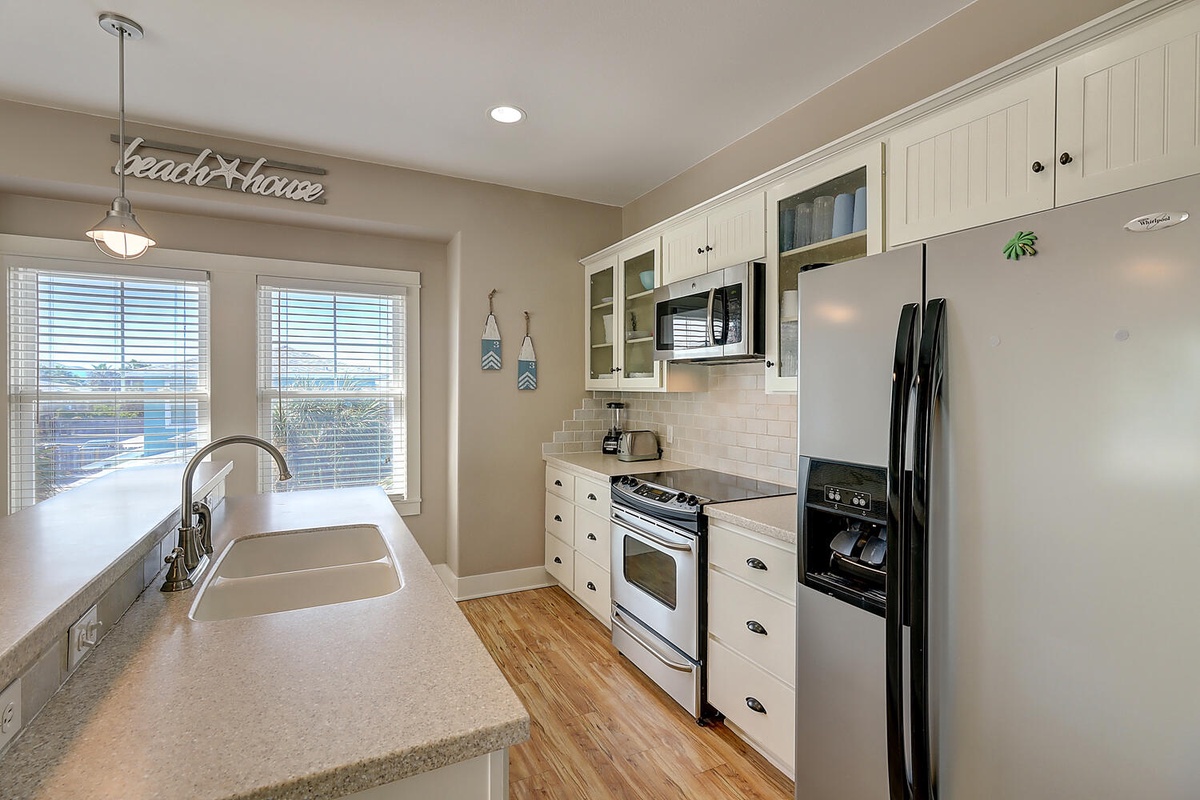 Your fully equipped beach house kitchen awaits, with granite counters and ocean views through bright windows.