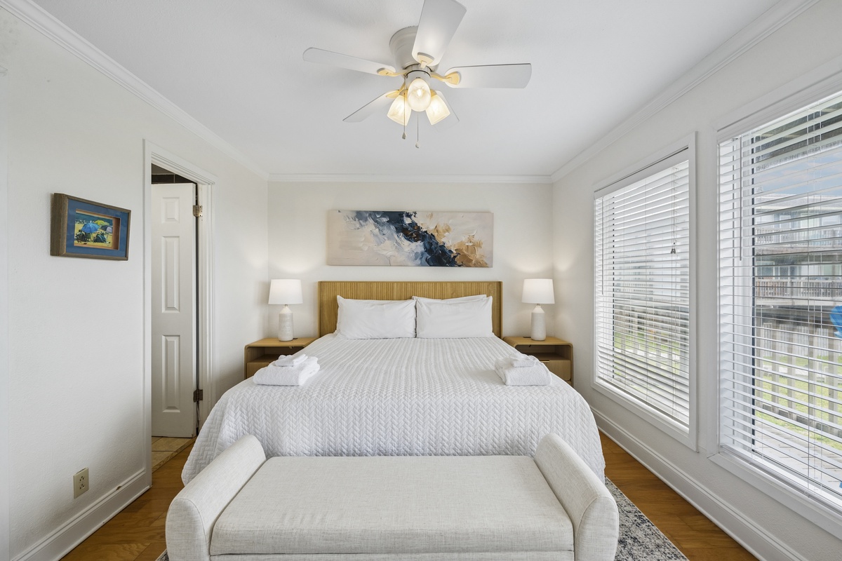 Slip into crisp white linens and unwind in your serene bedroom, where soft natural light and a gentle ceiling fan create the perfect escape for restful nights.