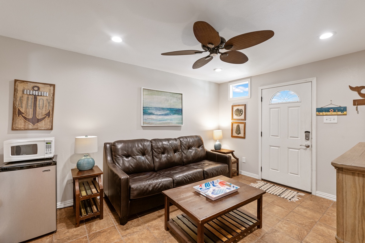 Sink into the plush leather sofa in your coastal-themed retreat, where ocean breezes from the ceiling fan and nautical touches create your perfect home base.