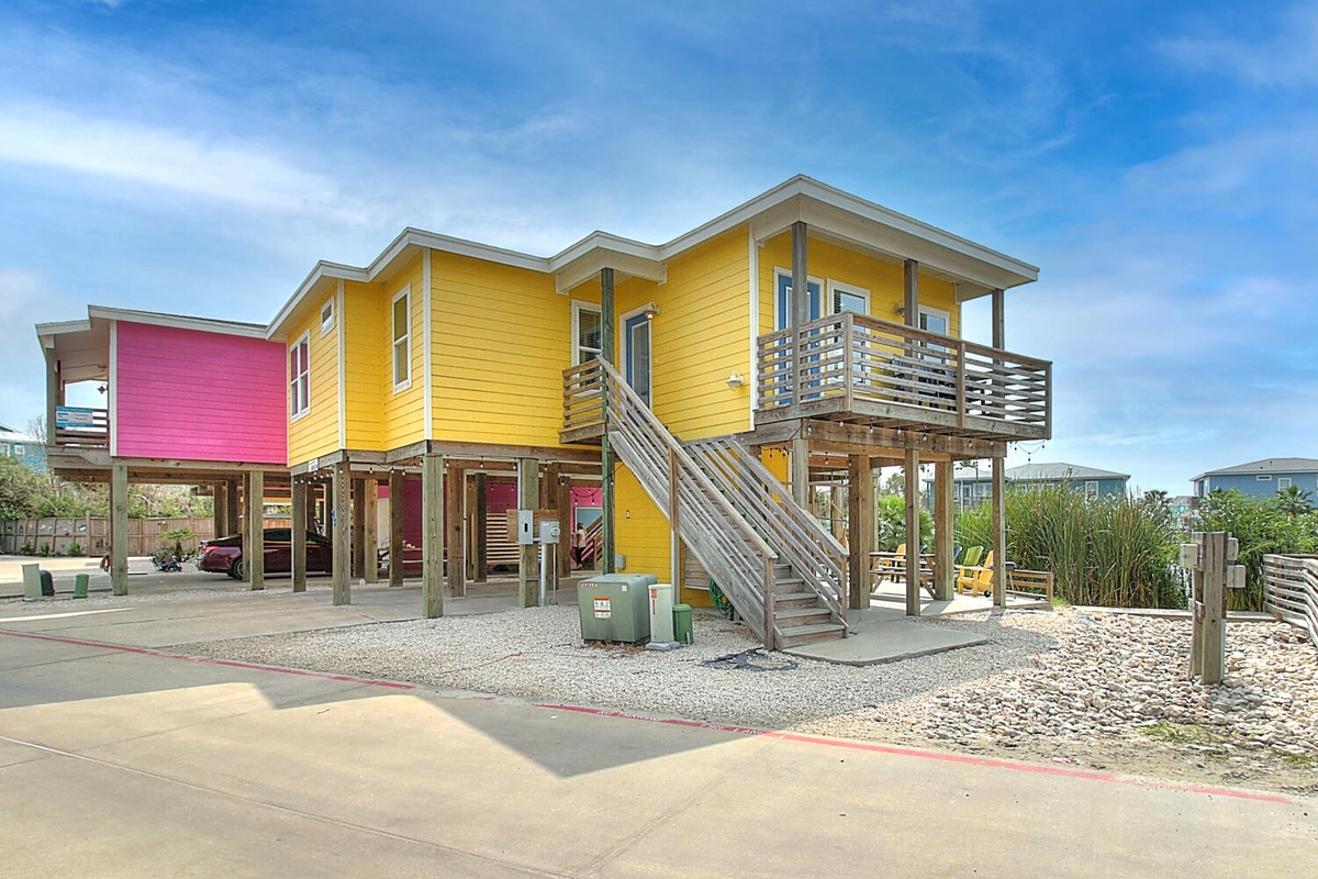 Colorful elevated beach houses featuring bright yellow and pink exteriors with wooden staircases and covered parking underneath.