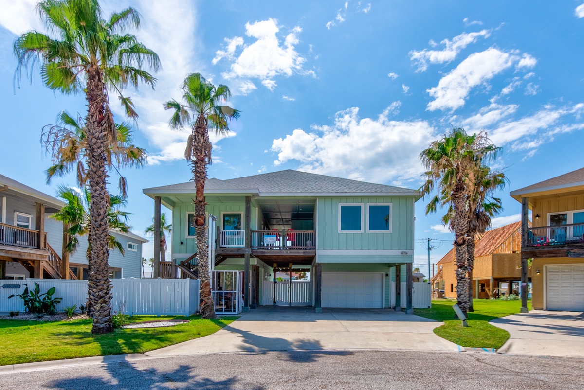 Charming coastal home with tropical palm trees and welcoming green siding in a peaceful neighborhood setting.