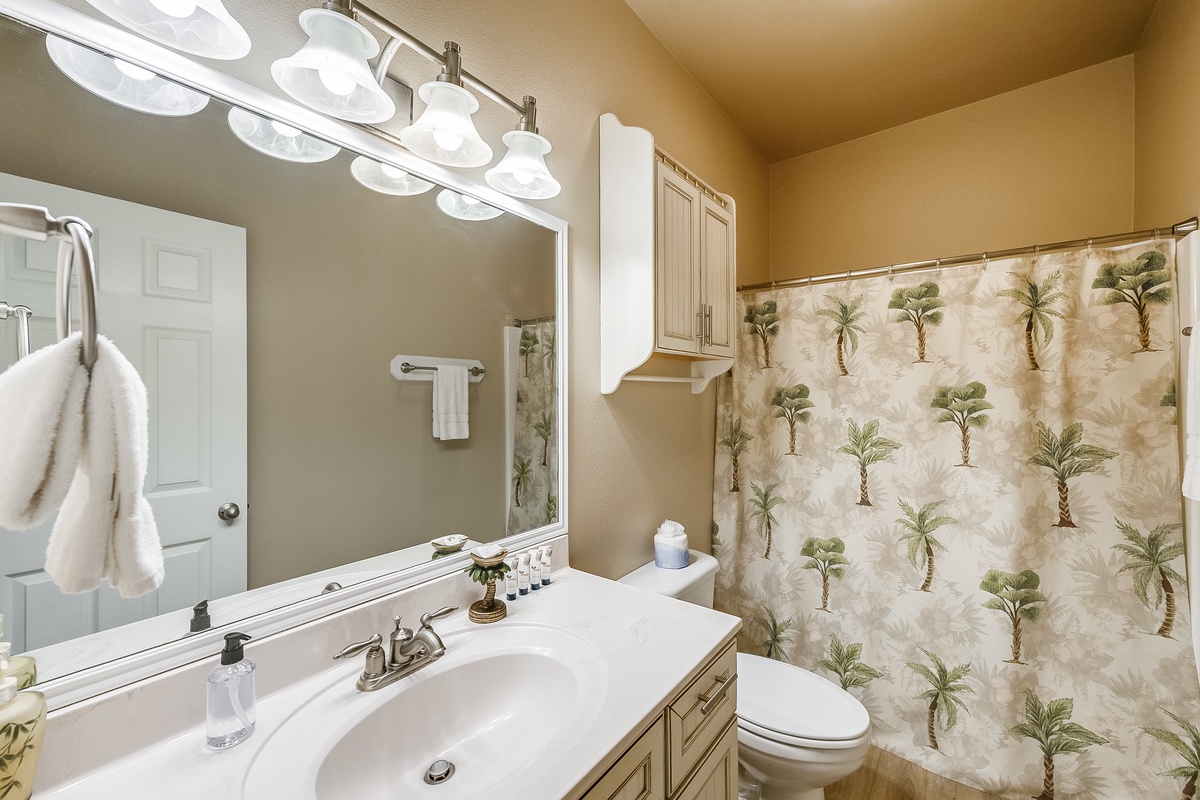Unwind in your private bathroom featuring warm lighting, tropical-themed shower curtain, and fluffy robes waiting for your relaxing retreat.