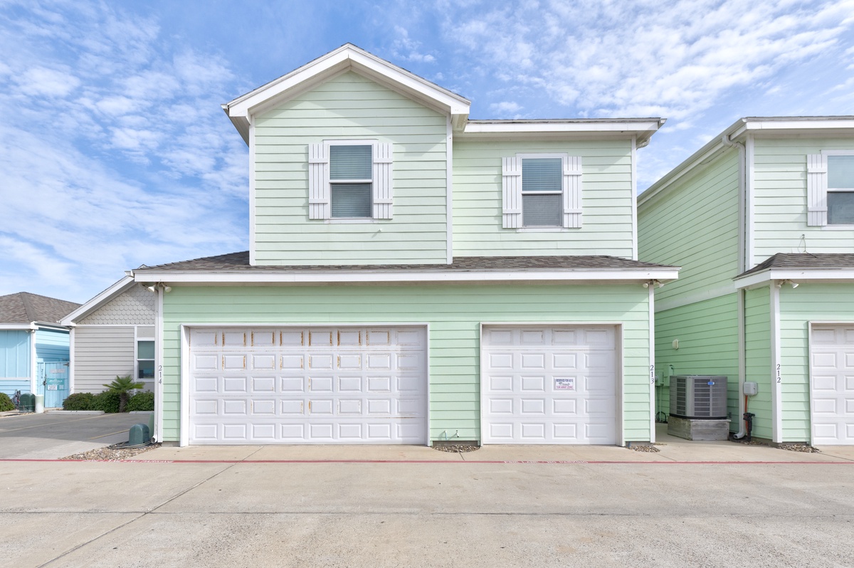 Charming mint green coastal-style townhouse with white shutters and spacious garage, nestled in a peaceful residential neighborhood.