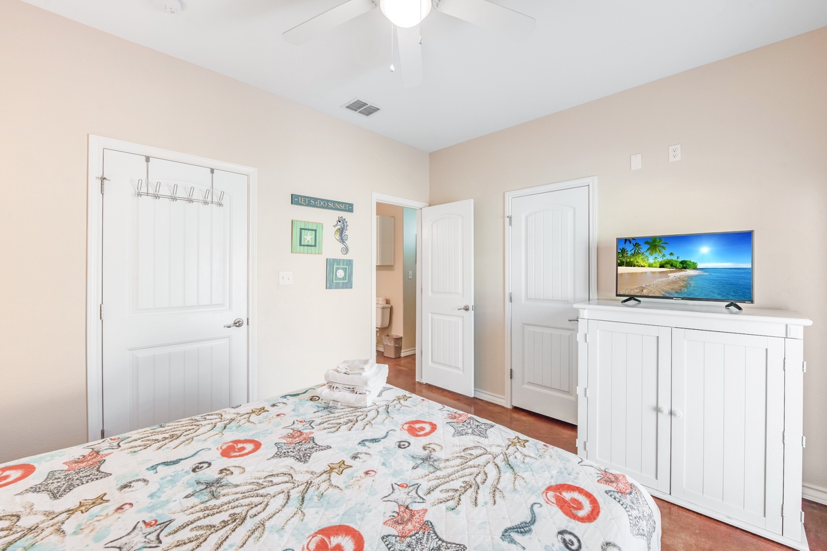 Relax in your cozy bedroom featuring a flat-screen TV, coastal décor, and ample storage with white furnishings creating a peaceful retreat.
