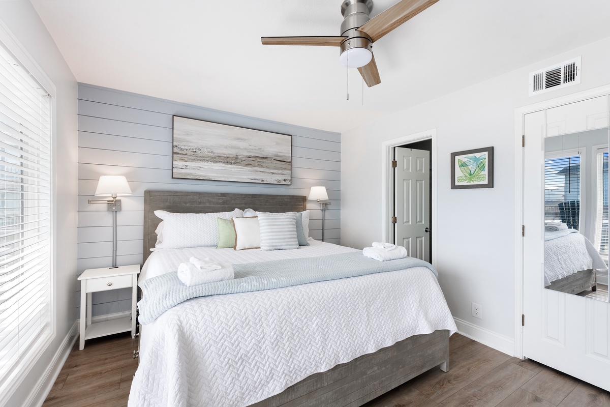 Drift off in this serene bedroom featuring coastal-inspired decor, plush linens, and gentle ceiling fan for your perfect night's rest.