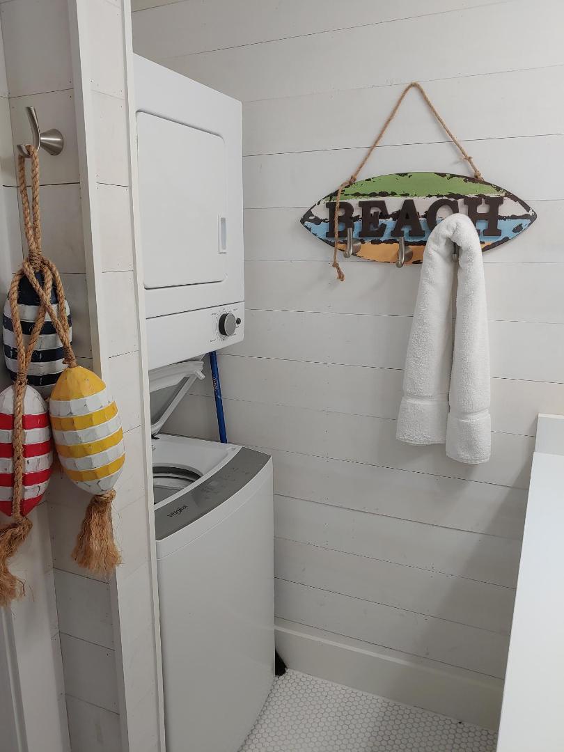 Your beachside laundry nook features a stacked washer and dryer with charming coastal touches like nautical rope details and fresh towels.