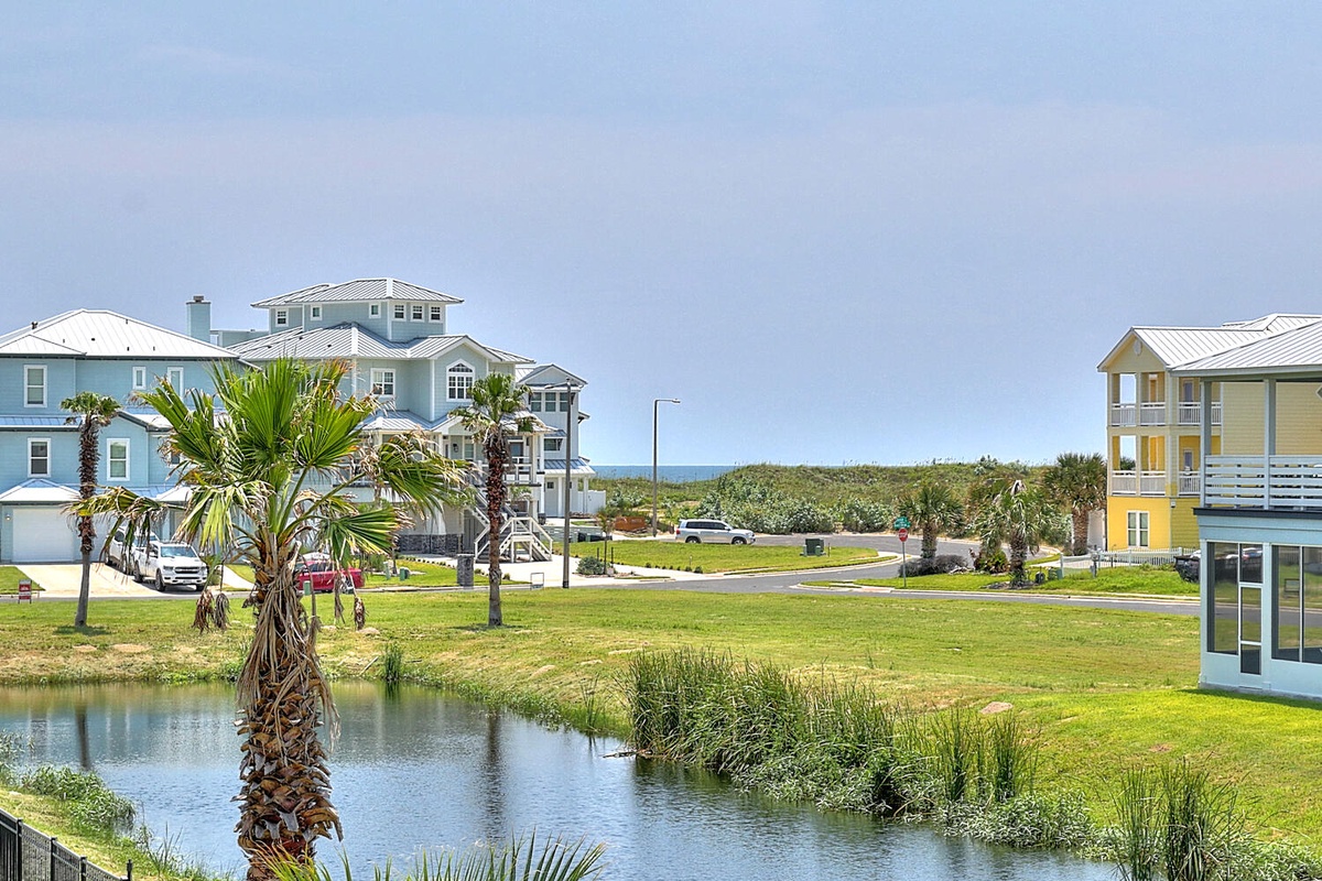 Colorful coastal homes surrounding peaceful pond create charming beachside community setting with palm trees and ocean proximity.