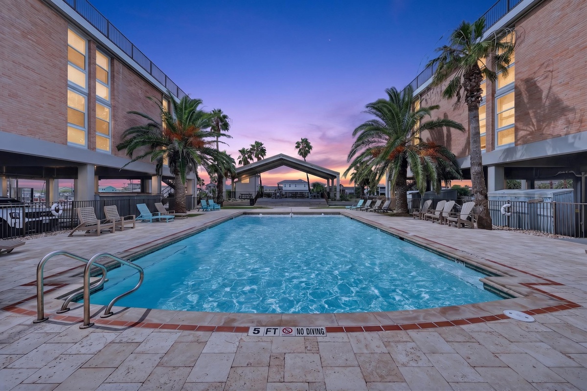 Picture yourself unwinding by the sparkling pool as the sky transforms into stunning shades of pink and purple. Palm trees frame your evening perfectly, while lounge chairs wait for you to settle in and soak up the peaceful ambiance.