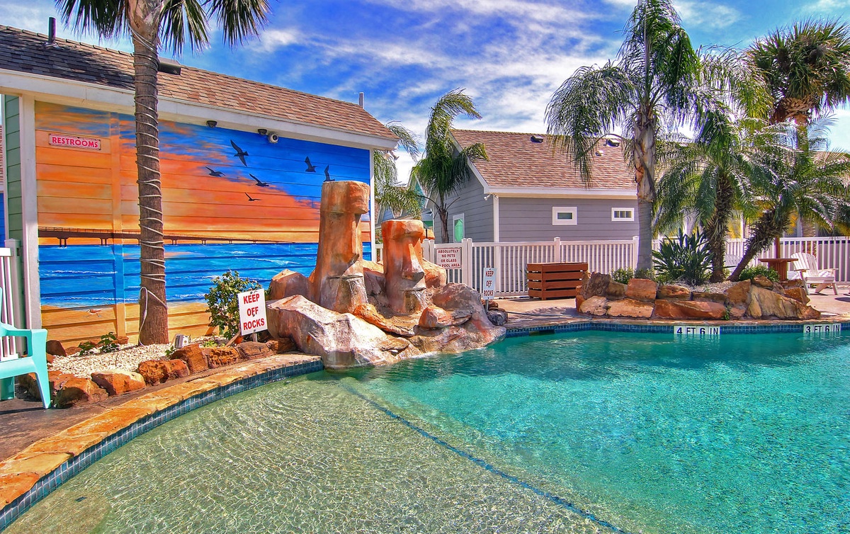 Tropical paradise awaits with crystal-clear pool, rock waterfall, and vibrant sunset mural creating your perfect island escape.