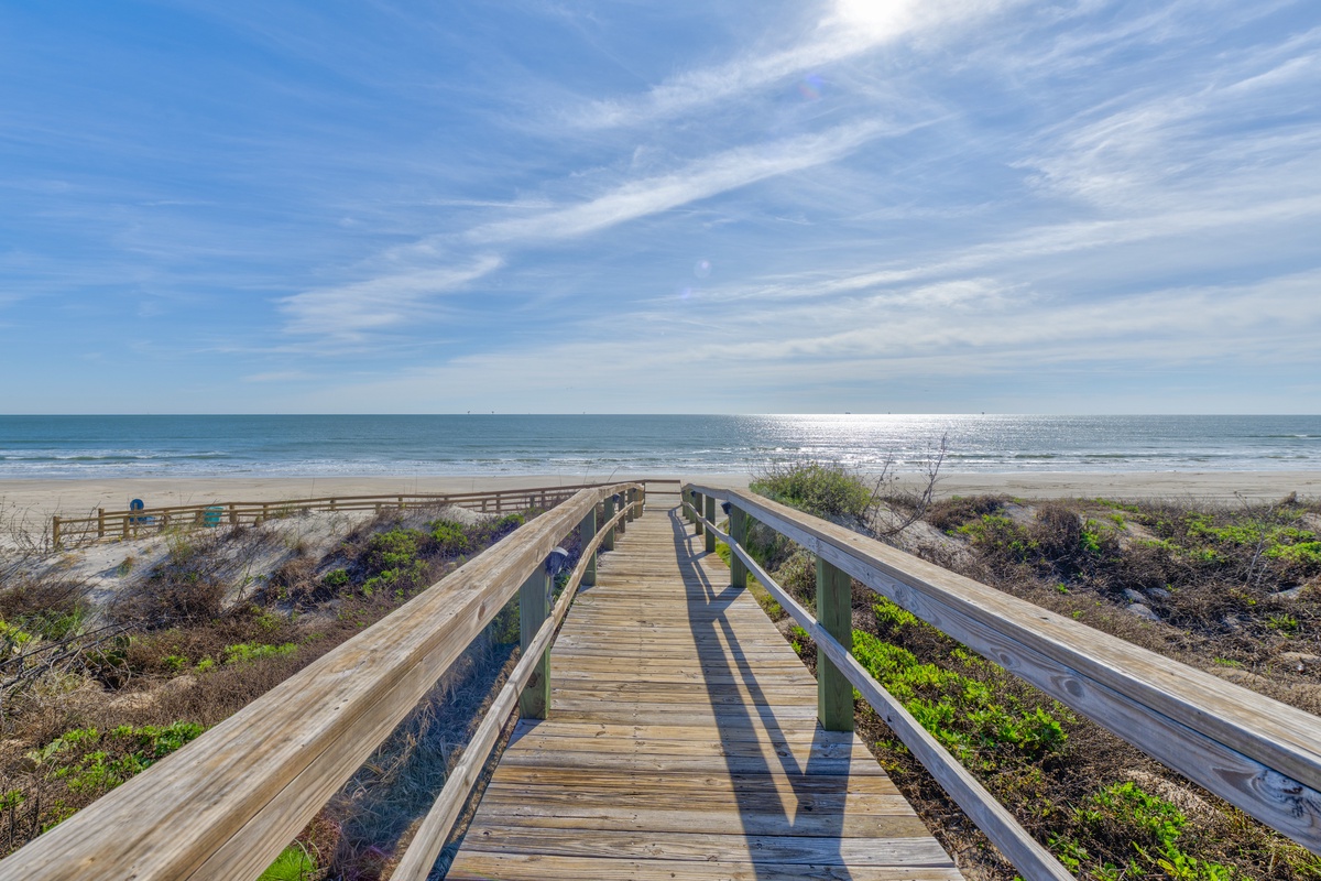 Wooden boardwalk leads directly to pristine sandy beach and sparkling ocean waters under beautiful blue skies.