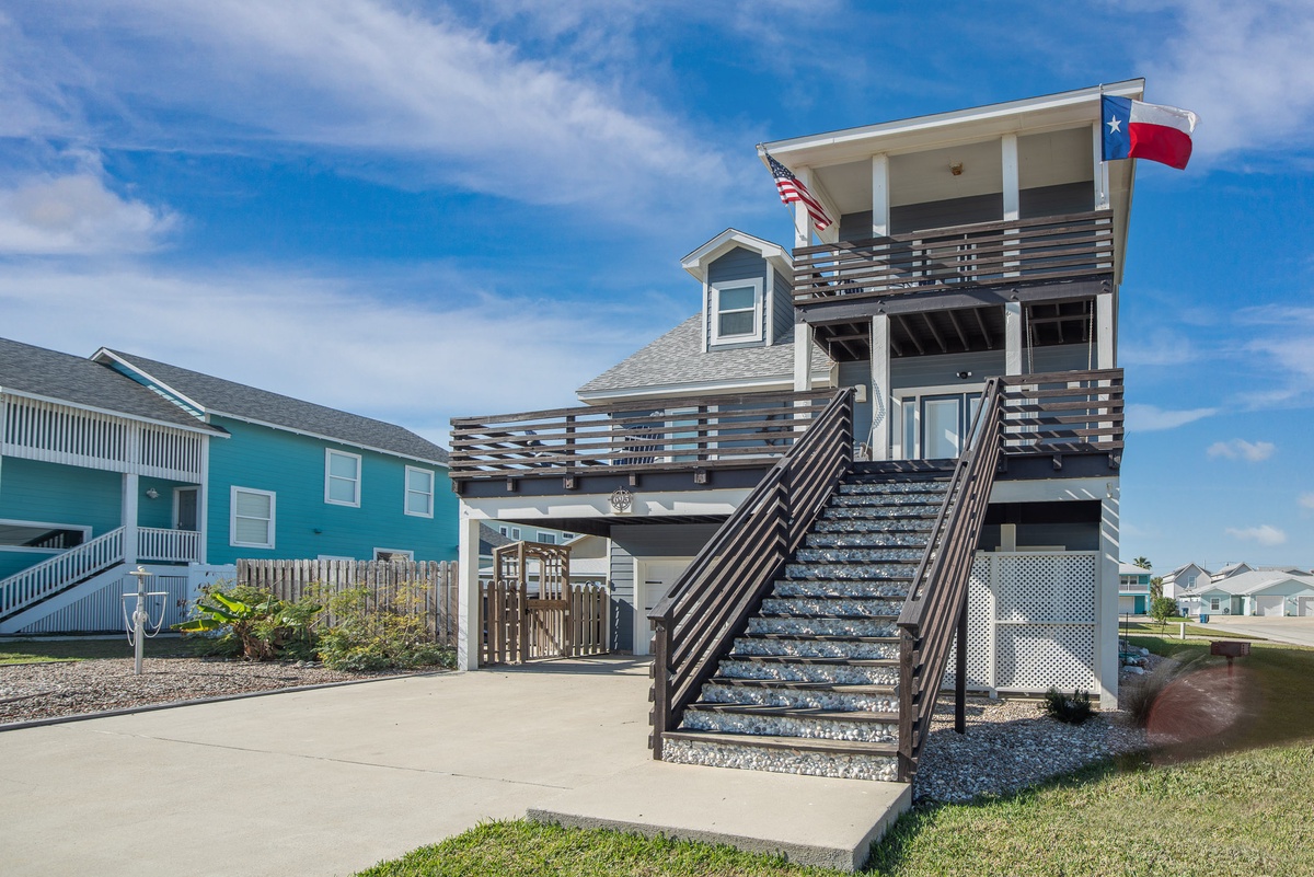 Contemporary coastal home with Texas flag and multiple deck levels in a relaxed neighborhood setting.
