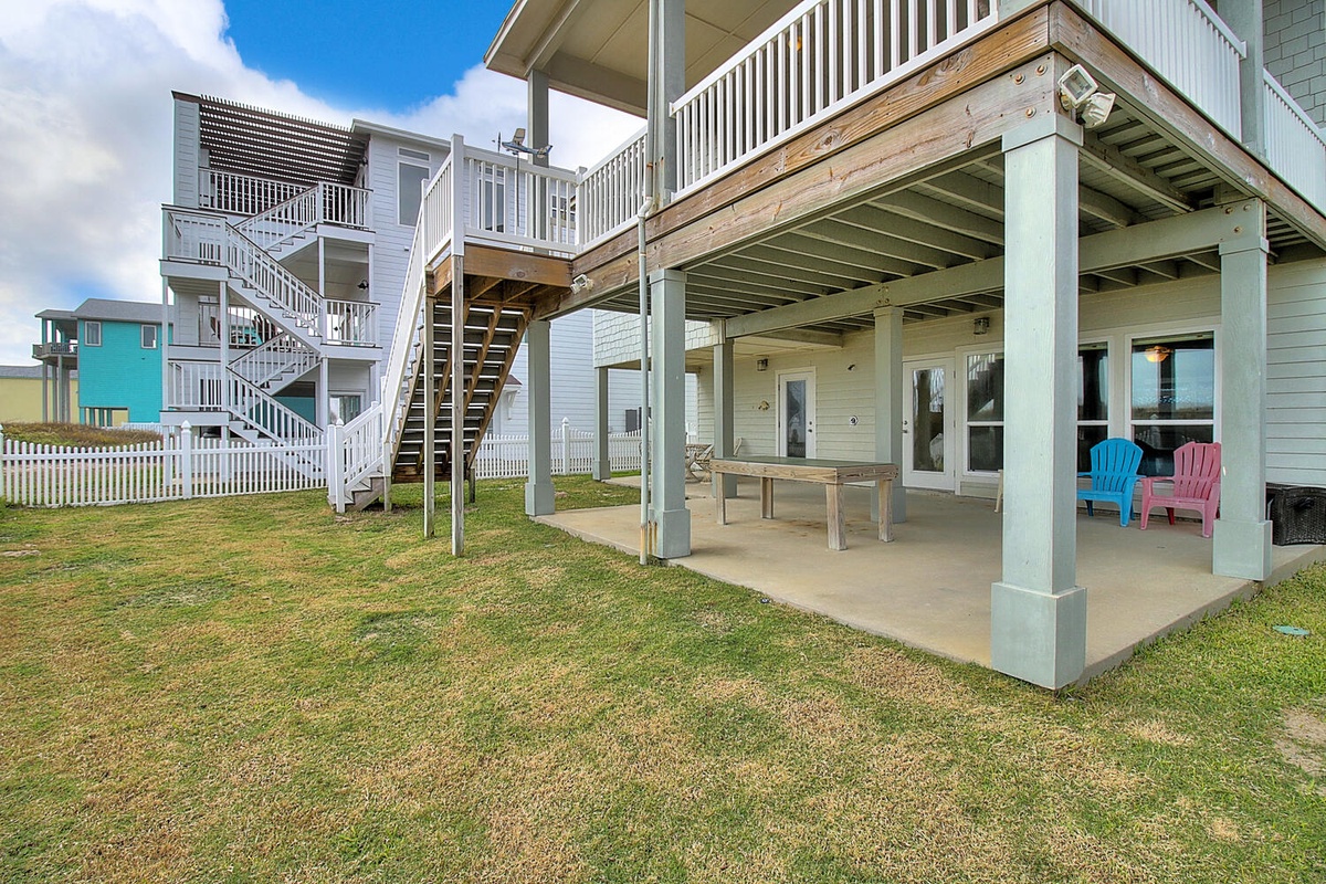 Multi-level beach house with covered patio and colorful chairs, surrounded by neighboring coastal properties.