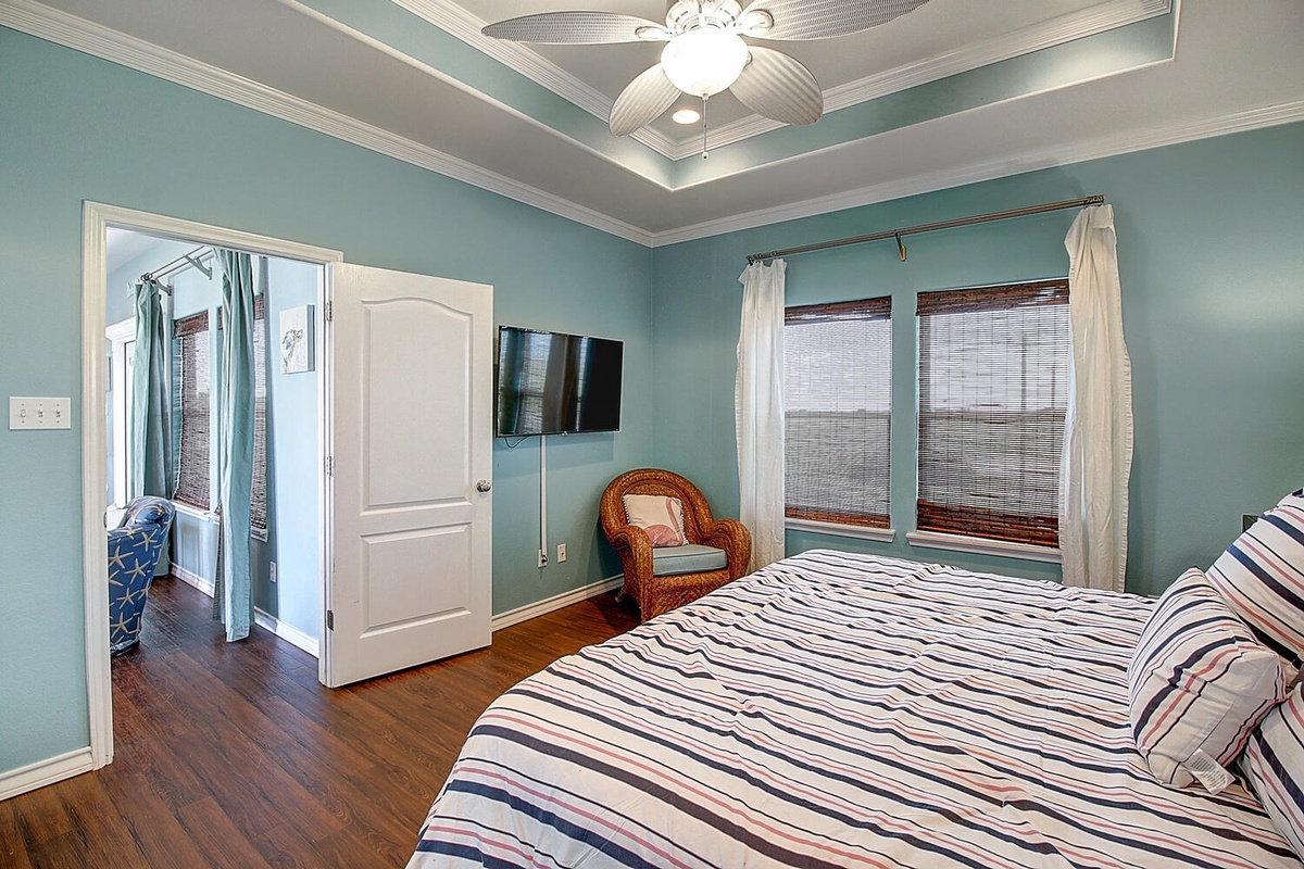 Drift off in your serene coastal bedroom with calming blue walls, ceiling fan, and private en-suite access for ultimate comfort.
