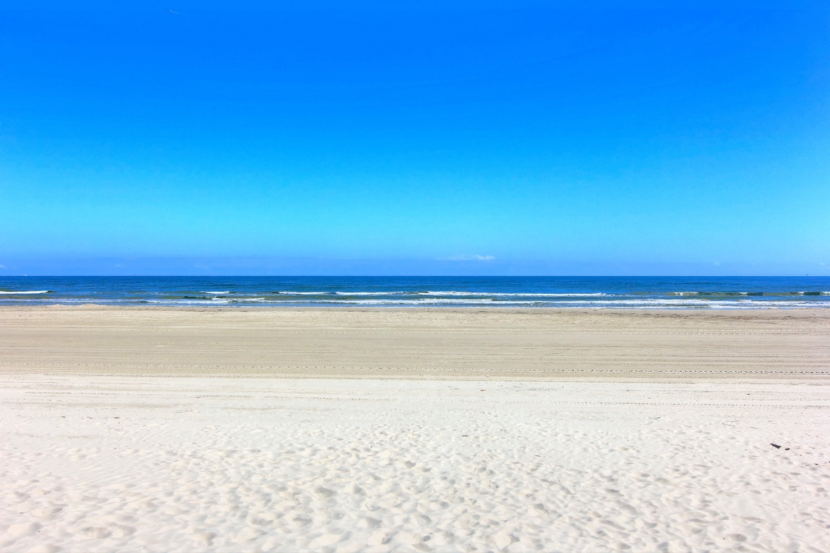 Pristine sandy beach stretches endlessly under brilliant blue skies, with gentle waves rolling onto shore creating the perfect coastal backdrop.