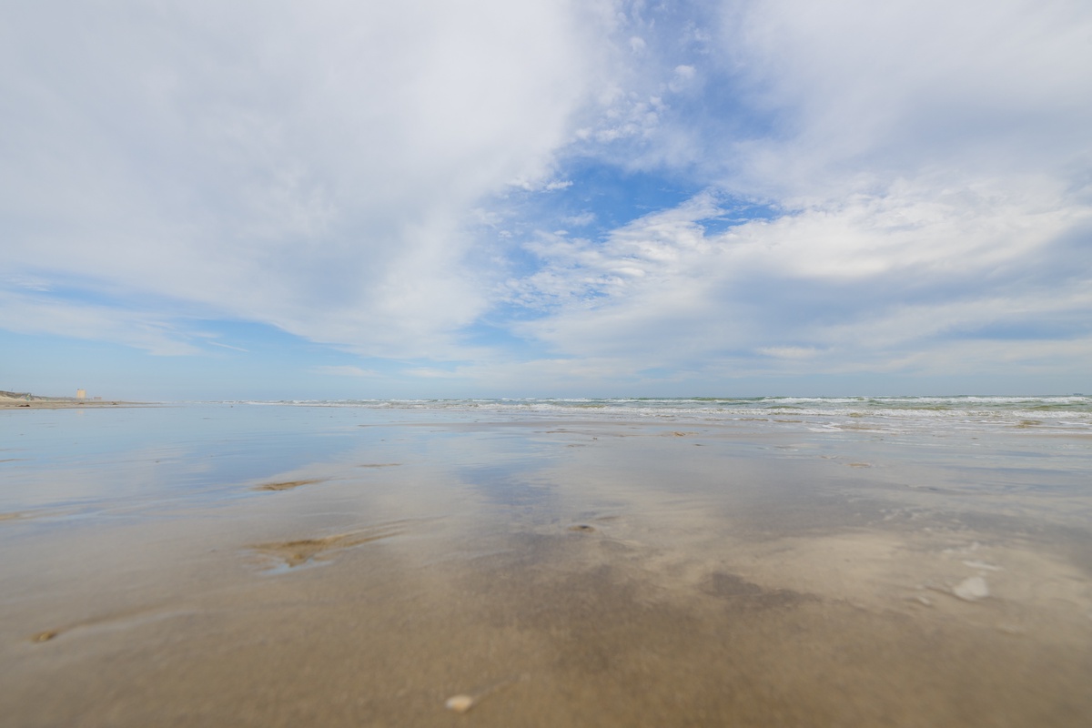 Pristine sandy beach stretches endlessly with gentle waves and dramatic cloudy skies creating a peaceful coastal atmosphere.