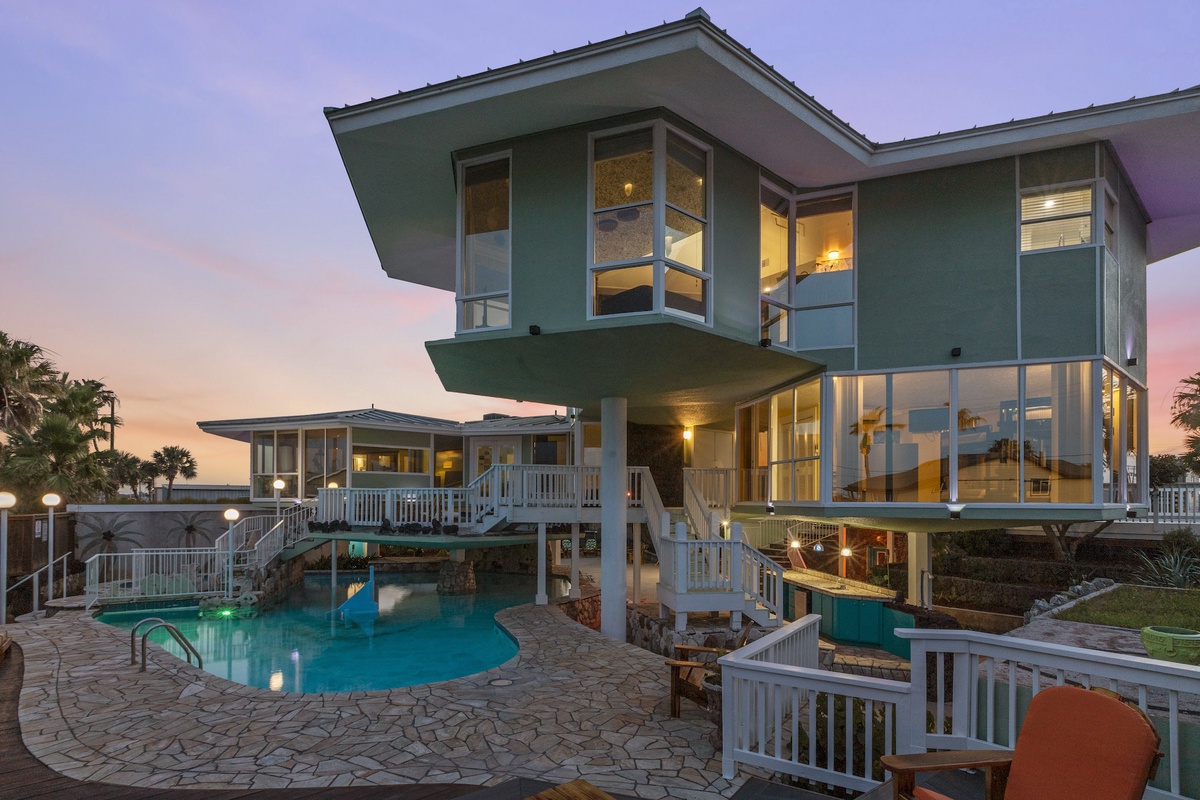 Modern beachfront villa with illuminated pool and spacious deck areas, perfect for evening relaxation.