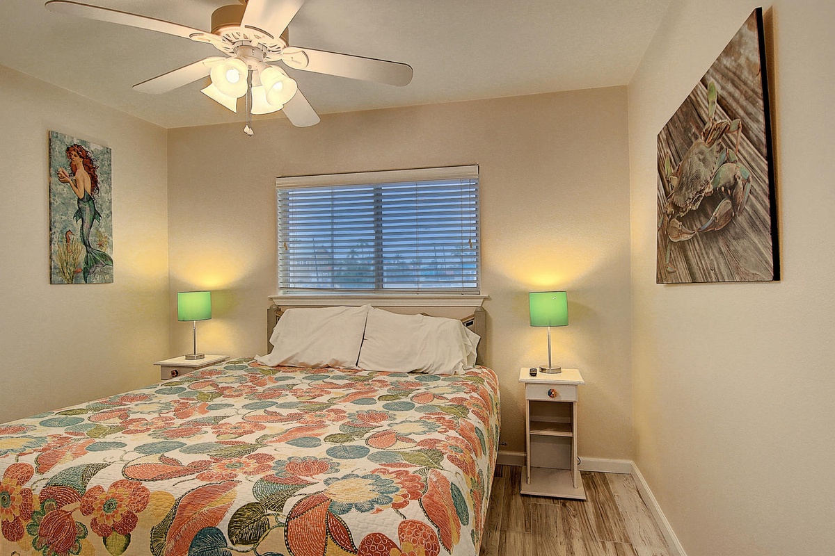 Drift off peacefully in your cozy bedroom with soft lighting, ceiling fan, and cheerful artwork creating the perfect atmosphere for rest.