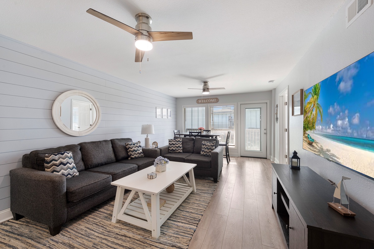 Sink into your comfortable sectional and unwind in this bright, coastal-inspired living space with shiplap walls and tropical artwork.