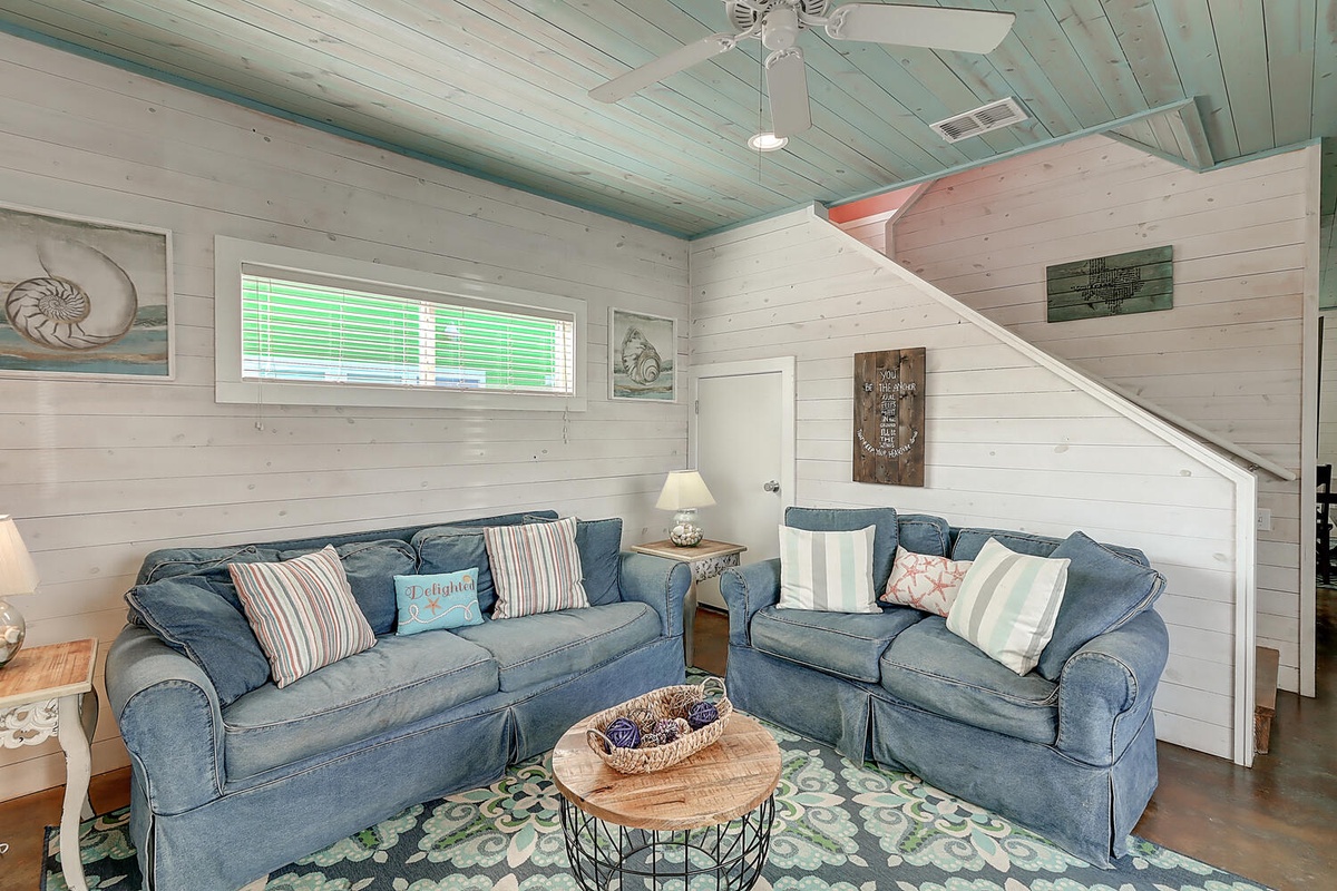 Relax in your coastal living room with comfortable blue sofas, charming nautical decor, and peaceful natural light streaming through the windows.