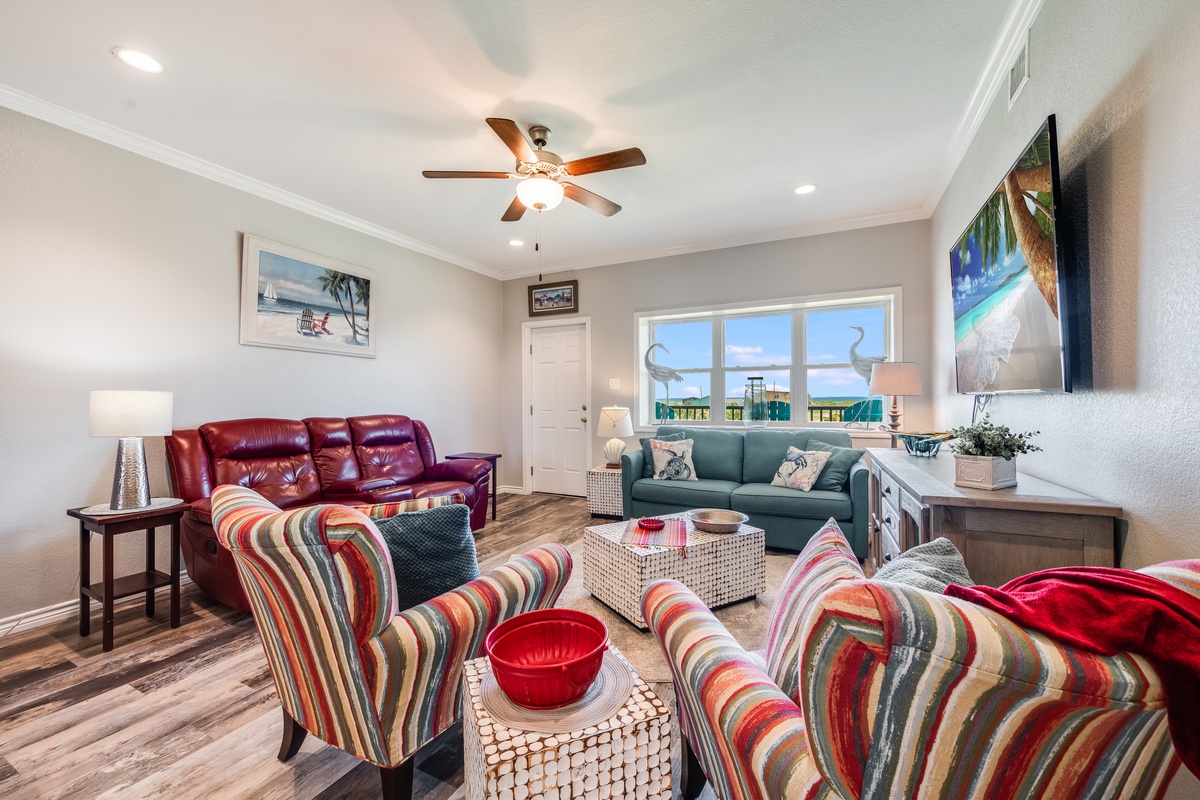 Unwind in your spacious living room with colorful seating, ceiling fan, and bright windows creating the perfect atmosphere for relaxation.