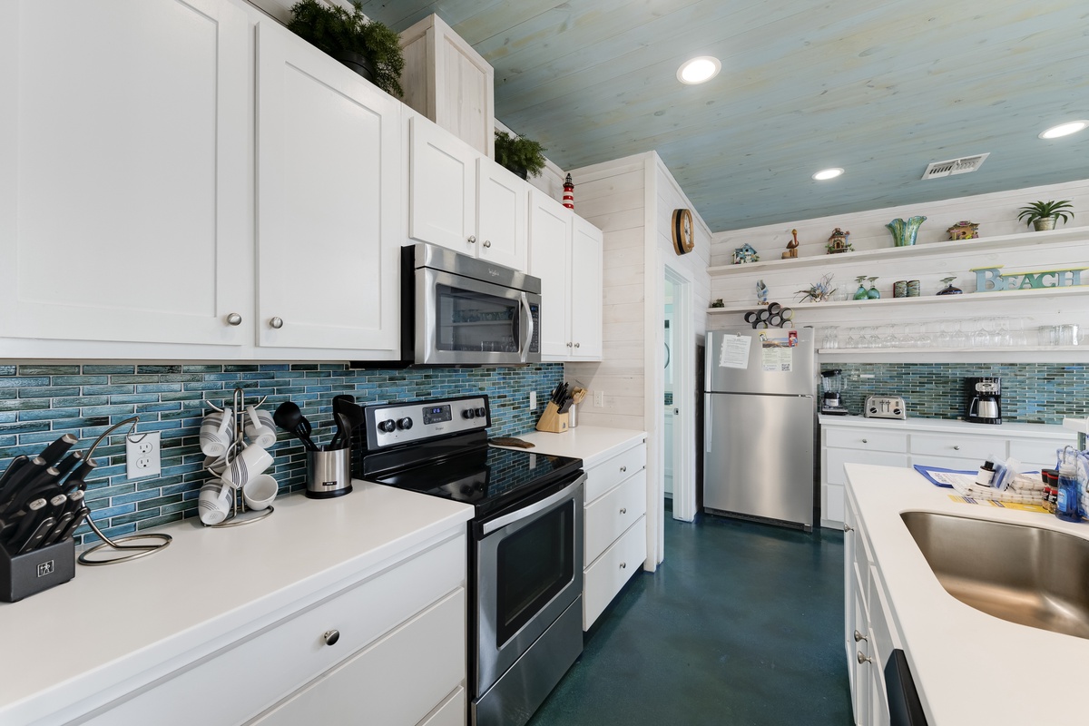 Your fully equipped kitchen features white cabinetry, ocean-blue tile backsplash, and stainless steel appliances perfect for preparing memorable meals.