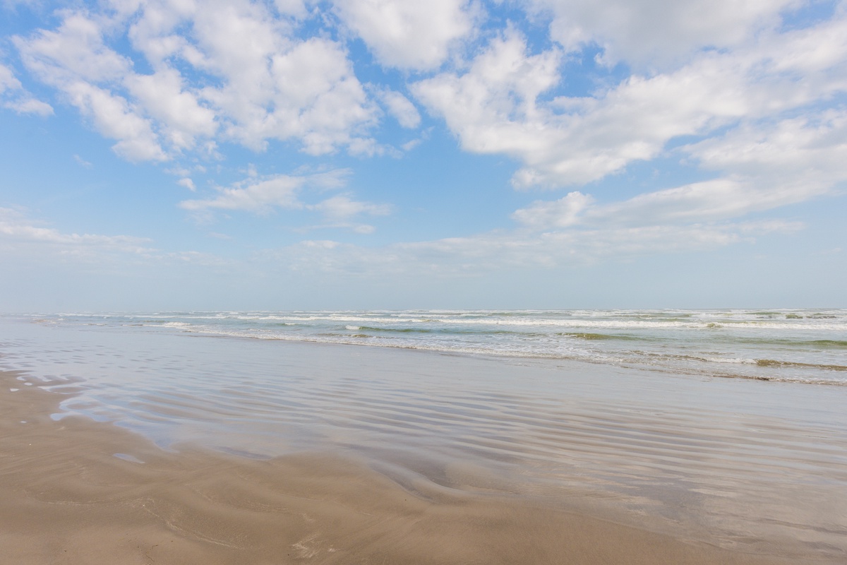 Soft waves meet sandy shores beneath expansive skies, offering peaceful coastal access just steps from the property.