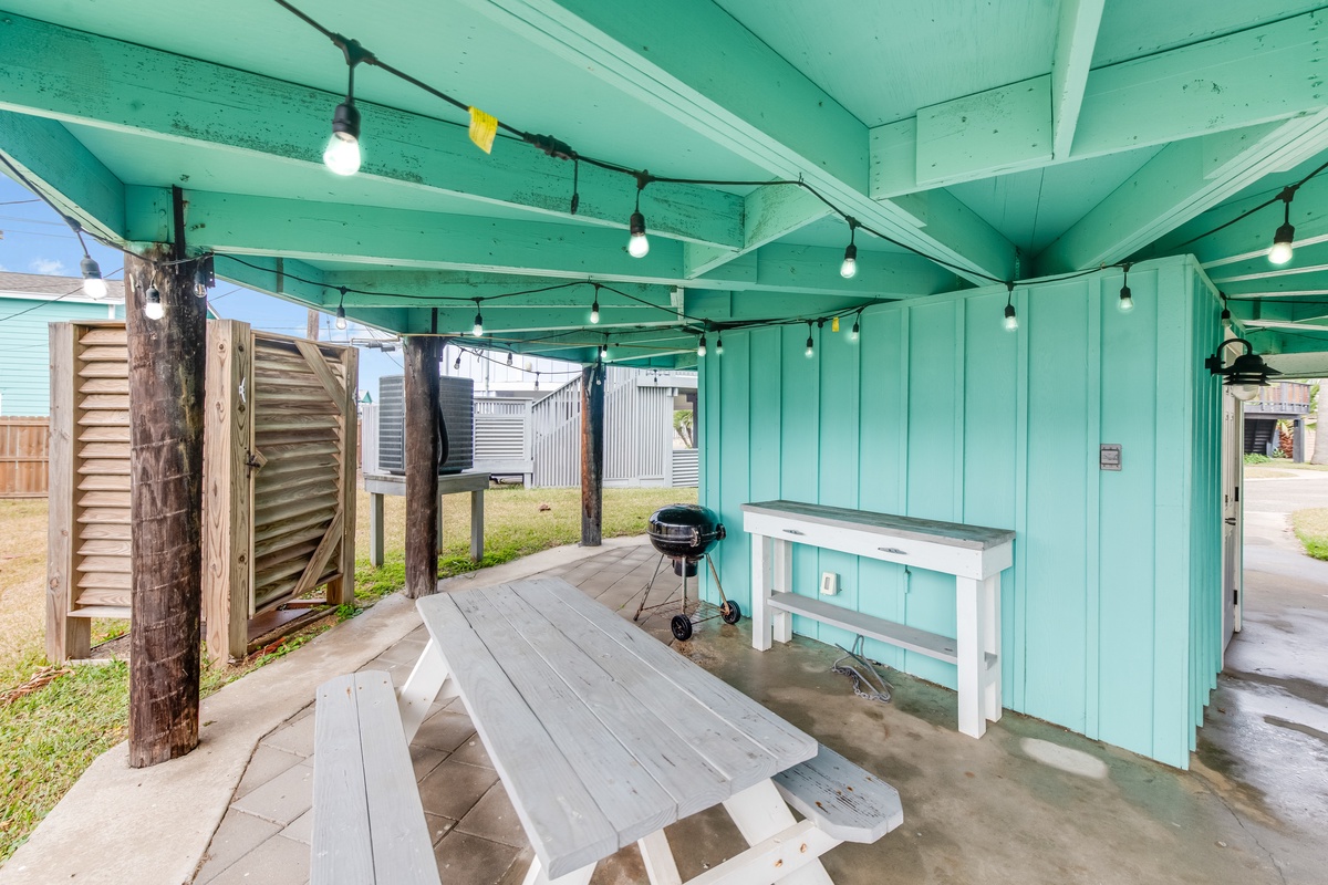 Your covered outdoor dining area features a picnic table, BBQ grill, and charming string lights for memorable evenings under the turquoise ceiling.