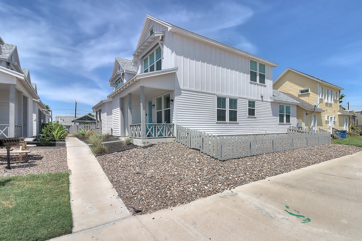 Charming coastal cottage with bright white siding and turquoise accents in a peaceful neighborhood setting.